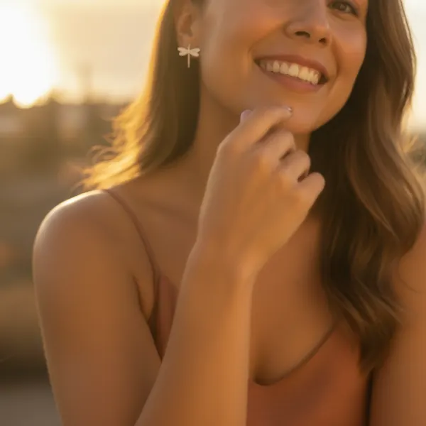 Close-up of a smiling model at golden hour wearing the silver dragonfly earring