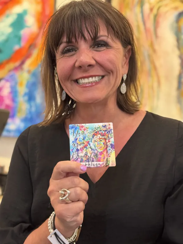 Una clienta muestra su cerámica MIA personalizada con el nombre Kathleen, con las pinturas de la galería brillando detrás