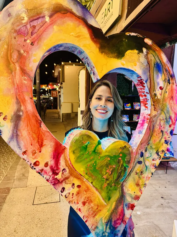 Una clienta sonríe a través de la escultura gigante de corazón pintado afuera de la galería, en el Distrito del Arte al atardecer