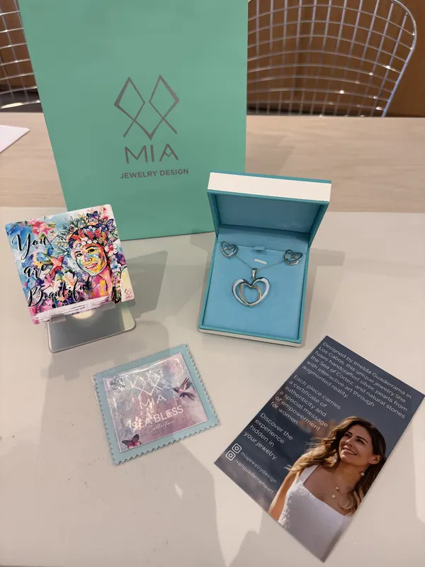 Flat lay of MIA packaging: turquoise gift bag, jewelry box with a ring, painted ceramic tile and brand cards